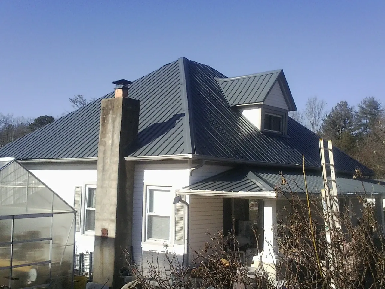 Dark blue standing seam metal roof on a white farmhouse with dormer — Slate & Tile Roof Repair by Roofing Brothers in Mineral Wells