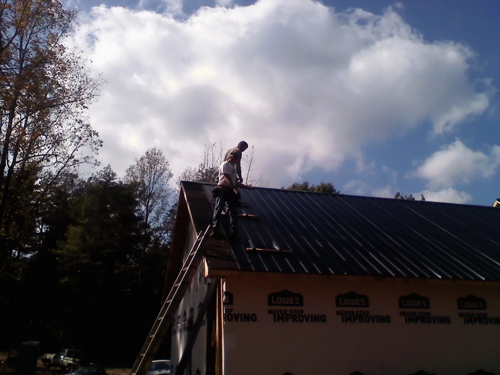 Roofer fastening dark metal panels high against a cloudy sky, from a Roof Inspection job in Mineral Wells